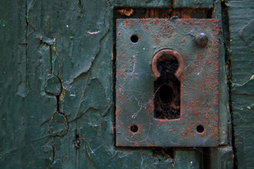 Close-up on old rusty metal lock. Green-painted key closure on a worn wooden door in a garden. Paint flaked.