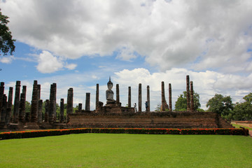 Buddha in the middle of many columns in a space with a lot of vegetation