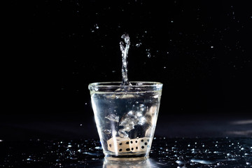 Obraz na płótnie Canvas vaso splash con agua fondo negro y dados