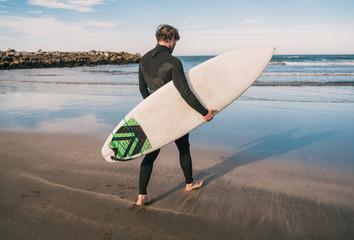 Surfer entering into the water with his surfboard.