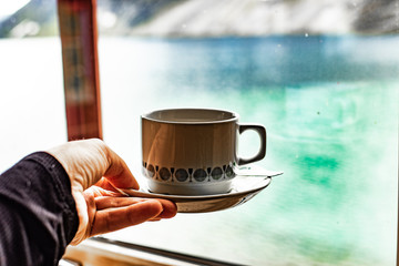 Coffee cup on saucer made of white ceramic with tiny black pattern. Hand keeps coffee cup....
