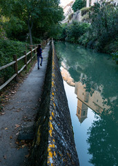 Niña saltando por sendero junto a canal de agua con reflejo invertido de campanario