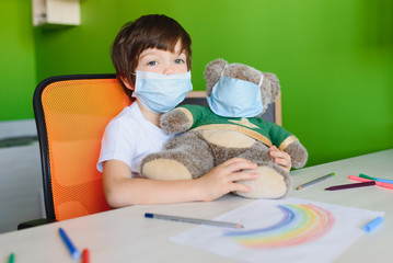 Stay at home due coronavirus pandemic concept. Close up little boy paints a rainbow on stay at home poster. Chase the rainbow flashmob. Positive activities during quarantine and staying at home.