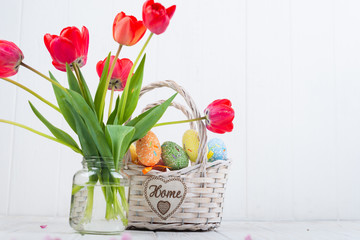 Multi-colored Easter eggs in a basket on a white wooden background