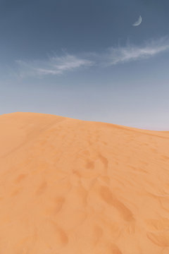 Giant sand dune in the desert and a blue sky with a sungle long cloud and the moon