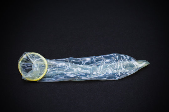 Unpacked condom on a black background, photo in dark or low key, toned