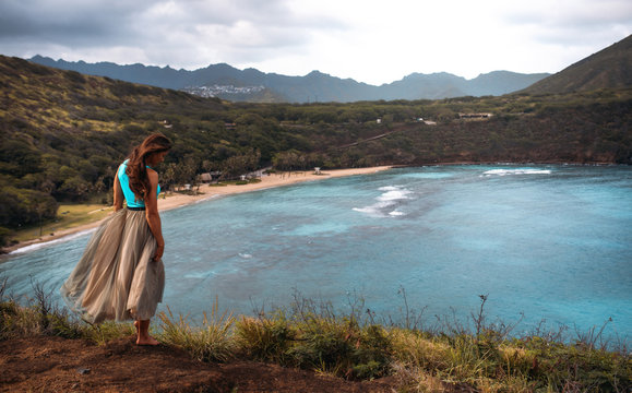 Hawaiian girl stay on the edge of a cliff with blue ocean and mountain on a background
