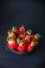 Fresh juicy strawberries in a black plate on a black matte background
