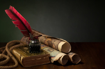 Quill pen, inkwell and old rolled up maps and papers