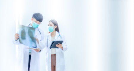 Blurred image, male doctor and female doctor standing wearing surgical mask  holding X-ray film and note plate. Two people wearing groundwear and stethoscope is consulting with copy space