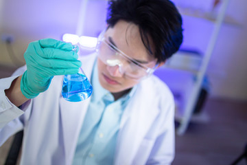 An Asian male scientist is watching blue liquid in a science test tube in a science lab.