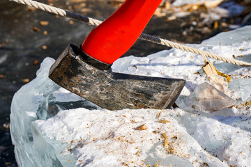 old ax with a red handle stuck in a snow block of ice, large, winter