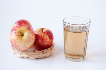 Three red apples in a wicker plate a glass of Apple juice on a white background