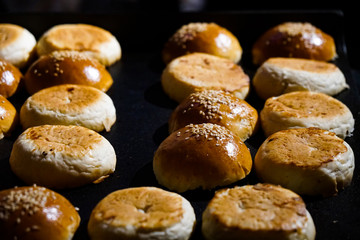 many sliced ​​buns with sesame seeds, fried on a black tray, culinary background