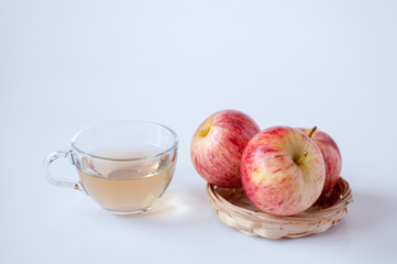 Three red apples in a wicker plate a transparent Cup of Apple juice on a white background