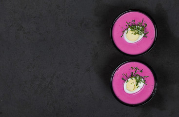 Cold beetroot soup with egg and parsley in a bowl on a dark gray background top view