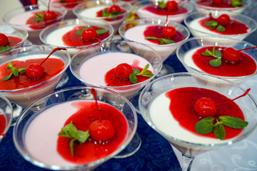 a lot of delicious white desserts, jelly in a glass with red jam, mint and cherry
