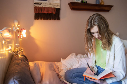 Teenage girl writing in journal in her bedroom at home