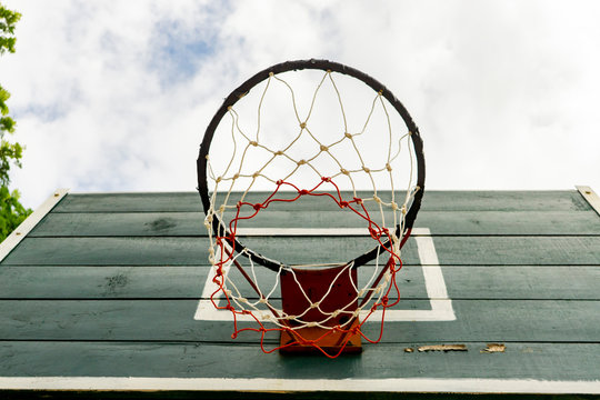 photograph of basketball hoop with wooden green board, shooting shot above looking at cloudy blue sky, representing reaching for achievement goals and aim high for success with journey and development