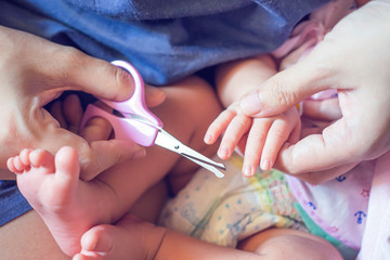 mom cutting new born baby nails using scissors, parenthood raising up child with love care and kindness comfort concept, mom looking after her infant, laying on bed resting sleeping on bed in bedroom