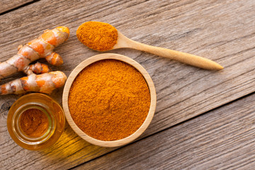 Tumeric powder ( curcumin, curcuma longa Linn) in wooden bowl and  spoon with root and bottle of turmeric essential oil extracted isolated on old wood table background. Overhead view. Flat lay.