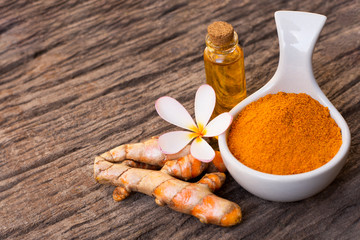 Tumeric powder and bottle of turmeric essential oil isolated on old wood table background. Beauty and spa concept.