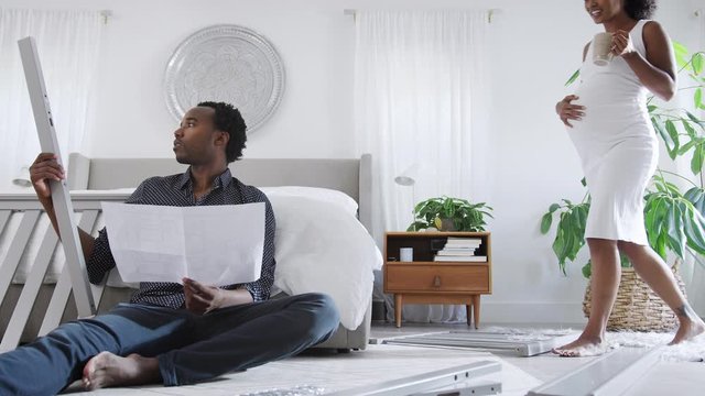 African American Couple With Pregnant Woman Look At Instructions For Building Self Assembly Baby Cot