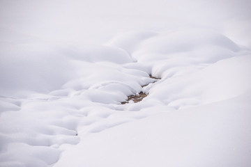 Valle ricoperta da un soffice manto di neve bianca fresca in cui scorre un piccolo ruscello 