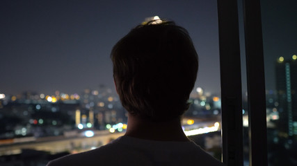 Sucessful Young Man Looking at City Skyline From High Rise Apartment Building at Night