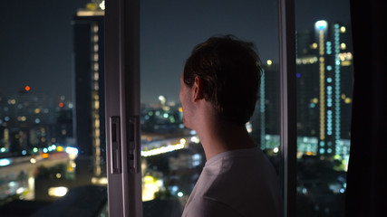 Smiling Man Looking Out A Window High Above The City at Night