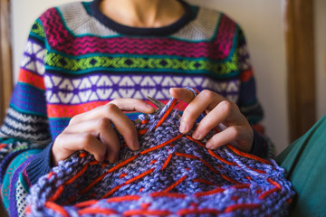 A woman knits from thick yarn, hands of a knitter.