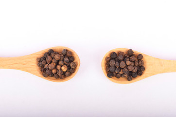 Black peppers on wooden spoon on white background.