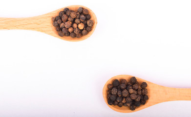 Black peppers on wooden spoon on white background.