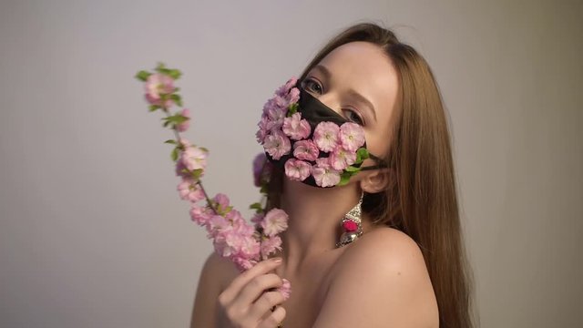 Girl with gorgeous long hair in an antiviral mask. Fashion video . Pandemic, virus, coronavirus, masked girl spring has come. Spring fashion, model in a mask of flowers with bloom.