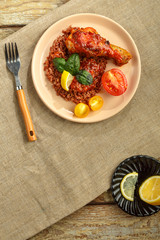 Chicken legs with red rice in tomato-garlic sauce on a plate and fork.