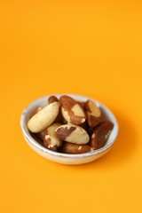 Brazil nut in a ceramic  cup on a bright orange Background. Wholesome food and snack. Healthy fats ingredient. Vegetarian and vegan food.keto diet. copy space.