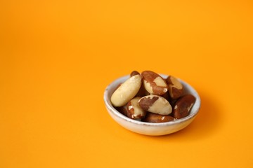 Brazil nut in a  cup on a bright orange Background. Wholesome food and snack. Healthy fats ingredient. Vegetarian and vegan food.keto diet. copy space.