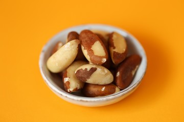 Brazil nut in a  gray cup on a bright orange Background. Wholesome food and snack. Healthy fats ingredient. Vegetarian and vegan food.keto diet. copy space.