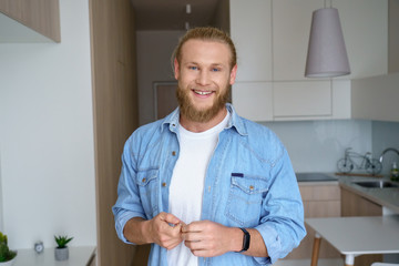 Smiling young bearded man tenant renter first time home owner holding key to new apartment looking...