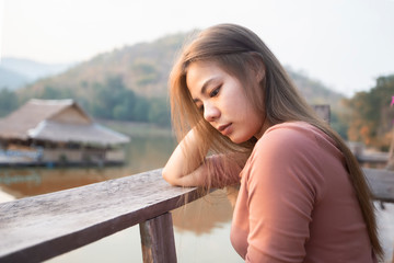 Portrait of asian girl are sitting on the wooden floor and looking the sunset over the mountain at rural Thailand. Beautiful asian women are looking view of nature.