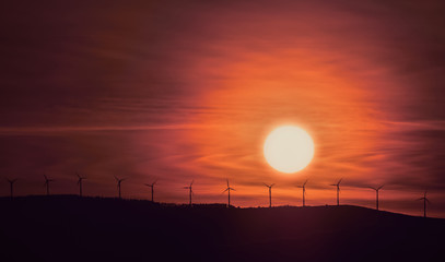 Sunrise with wind turbines on the hill and sun and clouds in the background