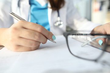 Close-up of female filling patient information on paper with silver pen. Medical worker in uniform and stethoscope equipment. Healthcare and modern medicine concept