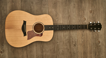 Full acoustic guitar laying down on a brown wooden floor