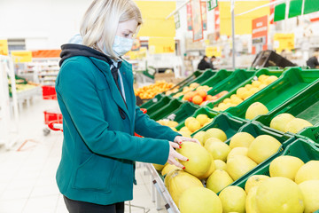 Woman with a mask on standing in an aisle at a supermarket picking fruit. The coronavirus outbreak forces people to stock up on fruits, vegetables and other foods and products.