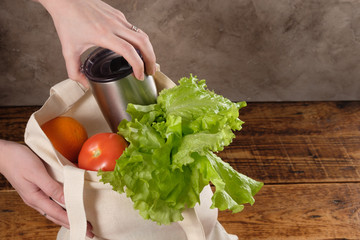 Eco-friendly groceries bag. Reusable shopping bag with fresh fruits and greens on wooden background. Bag , green salat, orange , tomatos on brown table. Healthy food, useful organic products.