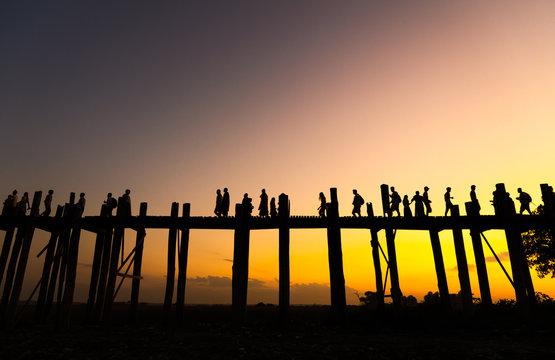 Twilight sunset scene of golden yellow sky, Burmese villagers walk across the U being Bridge in daily life