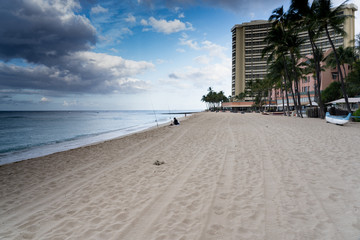 Waikiki Beach Hawaii opening day of the COVID pandemic. Few people, lone fisherman, diamond head, nearly empty beach a rainbow saying the beach is open.