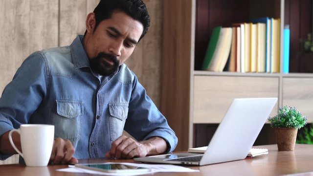 Asian young business man start up business at home or workplace,  smart entrepreneur or investor concentrate and calculate his business strategies on laptop technology, small business start up concept