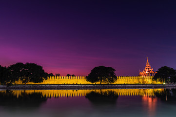 Fototapeta premium Dramatic night scene of most famous Royal Palace wall and trees reflect on water at Mandalay,Myanmar
