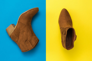 Top view of stylish suede boots on a yellow and blue background.